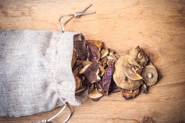 Dry mushrooms in sack on wooden table.