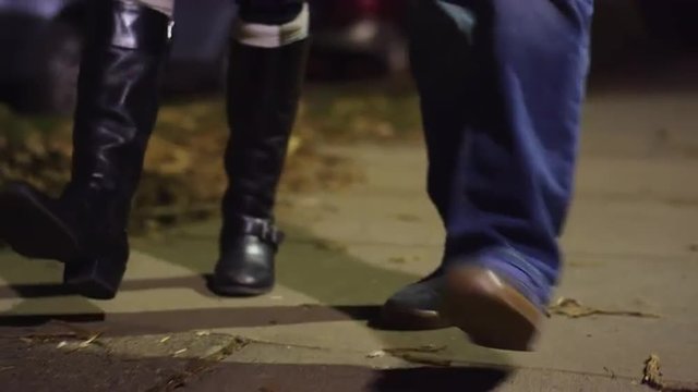 Two pairs of feet walking down a sidewalk at night