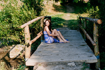 Beautiful young woman sits on wooden bridge in city park.