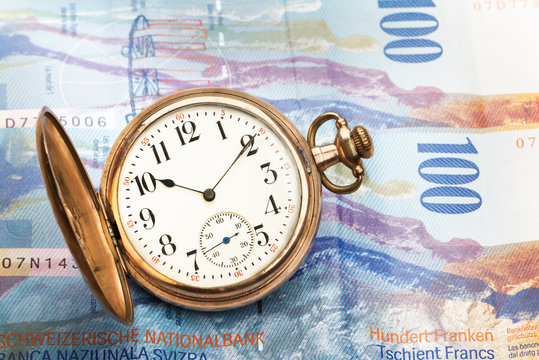 Time is money concept with hundred swiss franc bills and golden pocket watch.