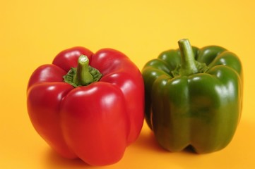 One red and one green pepper against a yellow background