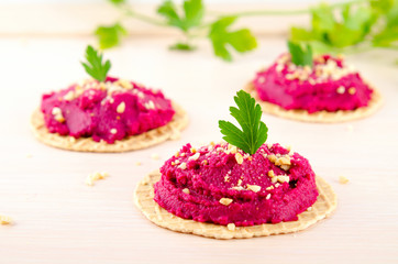 Beet hummus with peanuts and parsley on thin wafers