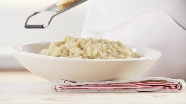 Risotto being sprinkled with parmesan and garnished with basil