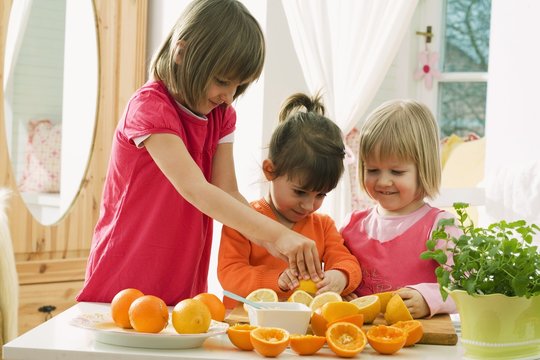 Three girls squeezing citrus fruit (for juice)