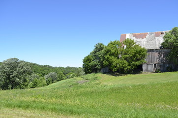 Fototapeta na wymiar Worn and weathered old barn on a hillside with trees