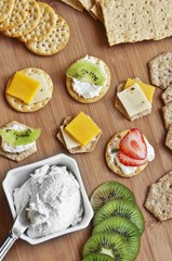 Assorted crackers on a cutting board with cream cheese, cheddar cheese kiwi and strawberry