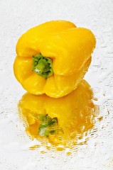 A yellow pepper on a wet mirror