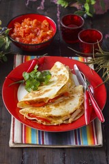 Two tortillas with chicken strips on a red plate on a colourfully striped placemat with a chilli dip in the background