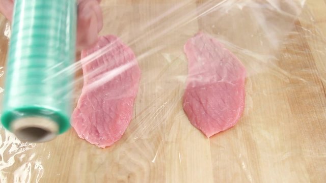 Veal escalopes being tenderized in cling film