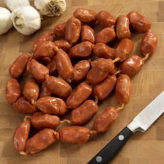 Spanish Spicy Small Link Sausages on a Cutting Board; Knife