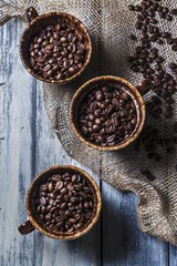 Three Cups of Coffee Beans on a Wooden Table with Burlap; From Above