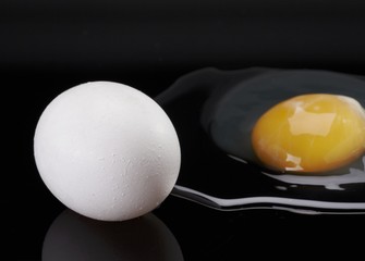 A whole egg and a raw egg out of its shell, against a black background