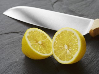 A halved lemon with a knife on a slate slab