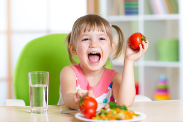 happy child eats dinner and shows tomatoes