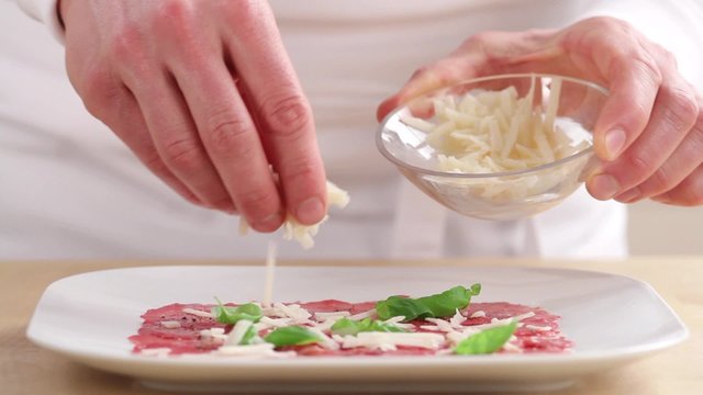Beef carpaccio being sprinkled with freshly grated parmesan