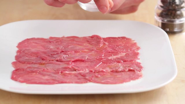 Beef carpaccio being seasoned with salt and pepper