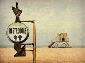 aged and worn vintage photo of lifeguard tower on beach sand and restroom sign