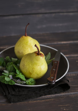 fresh pears and mint on a brown plate on a dark wooden surface