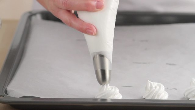 Meringue dots being piped onto a baking tray lined with greaseproof paper