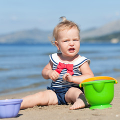 Happy cute girl in swimsuit playing with sand on beach