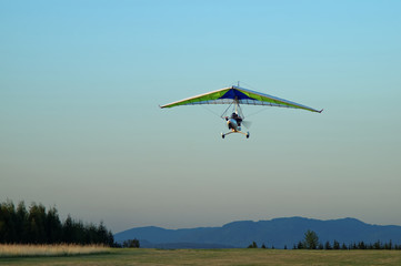 Hang glider flying over the landscape in the early evening.