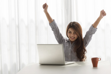 Excited woman raising her arms while working on her laptop in her home