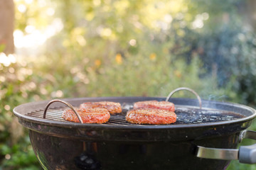 Raw beef burgers sizzling on a charcoal BBQ outdoors on a hot summer day 