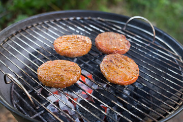 Four beef burgers sizzling on a charcoal BBQ with glowing red charcoal