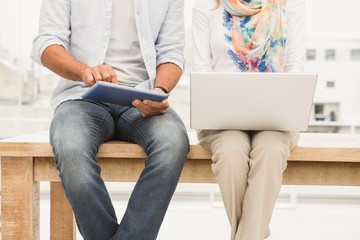 Casual designers sitting on wooden desk and using devices