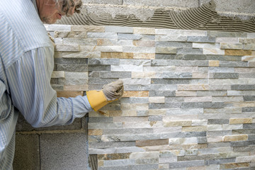 Older man decorating a wall with ornamental tiles