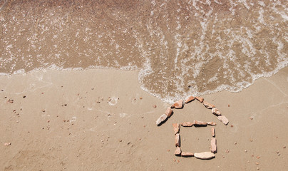 little house drawn in the sand of sea beach