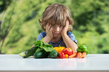 Cute little boy sitting at the table, unhappy with his vegetable meal, bad eating habits, nutrition...