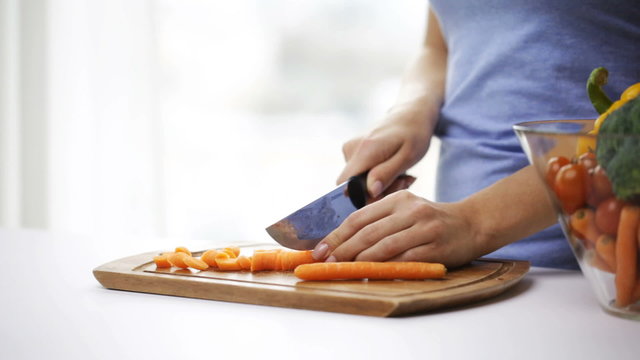 close up of young woman chopping carrot at home
