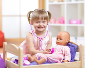 baby plays in doctor with toy doll and stethoscope