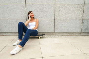 Fototapeta na wymiar Young girl siting on skateboard in the city talking by phone nea
