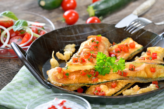 Krosse, panierte Zucchinischnitzel mit scharfer Dip-Soße und Tomatensalat serviert