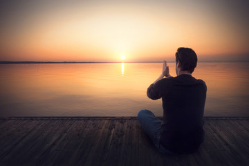 Man praying on a boardwalk at sunset