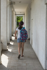 Teenage school girl with a backpack on her back and headphones. back view