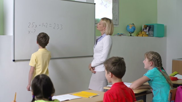 Math teacher calling a schoolboy to whiteboard to do the sums 