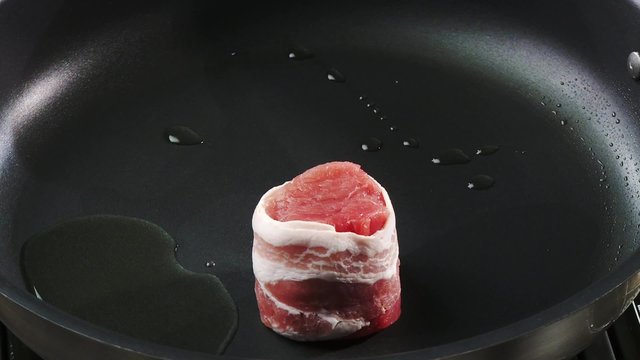 Frying barded pork medallions in a frying pan