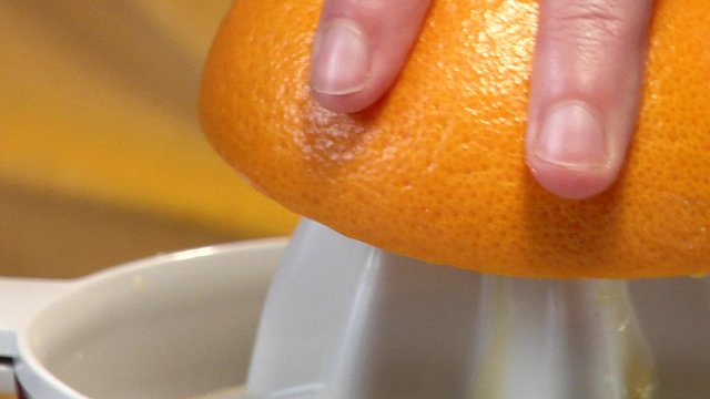 Squeezing an orange with an electric citrus squeezer (close-up)