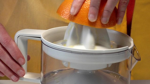 Squeezing an orange with an electric citrus squeezer