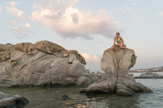Sexy model posing sitting on top of a rock  at Kolimpithres beach in Paros island in Greece.