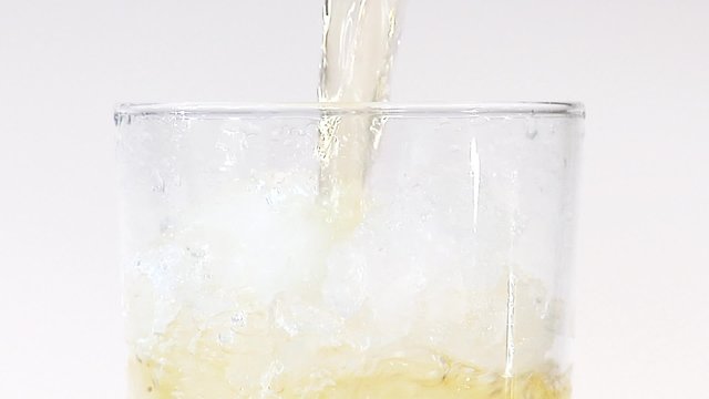 Pouring apple juice into a glass of crushed ice (close-up)