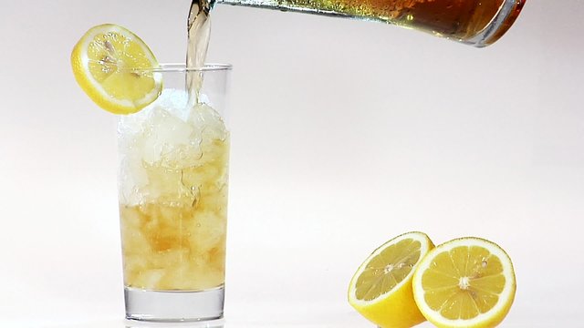Pouring apple juice into glass of crushed ice with slice of lemon