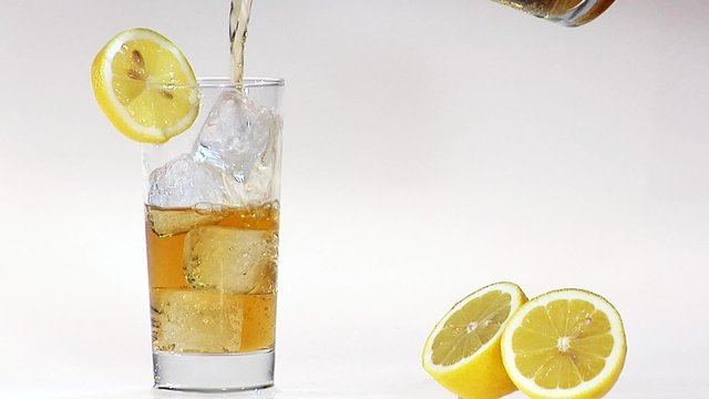 Pouring apple juice into glass of ice cubes with slice of lemon