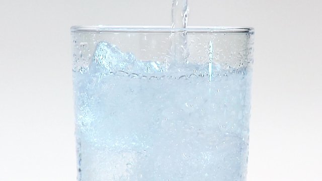Pouring mineral water into a glass of ice cubes (close-up)