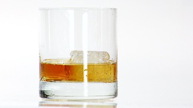 Pouring whisky into a glass with one ice cube