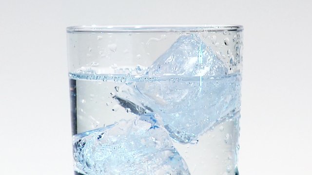 Pouring water into a glass of ice cubes (close-up)