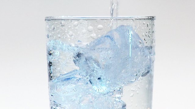 Pouring water into a glass of ice cubes (close-up)